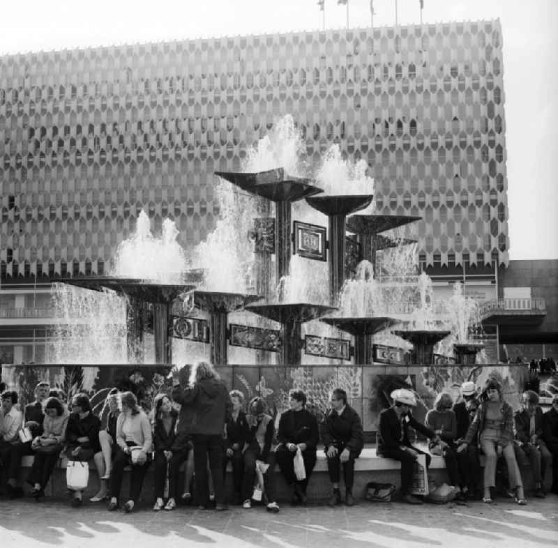 Tourists in front of the Fountain of International Friendship in Alexanderplatz in Berlin, the former capital of the GDR, German Democratic Republic. The fountain designed Walter Womacka under the redesign of Alexanderplatz. In the background the Centrum department store Galeria Kaufhof now stands with its aluminum honeycomb facade