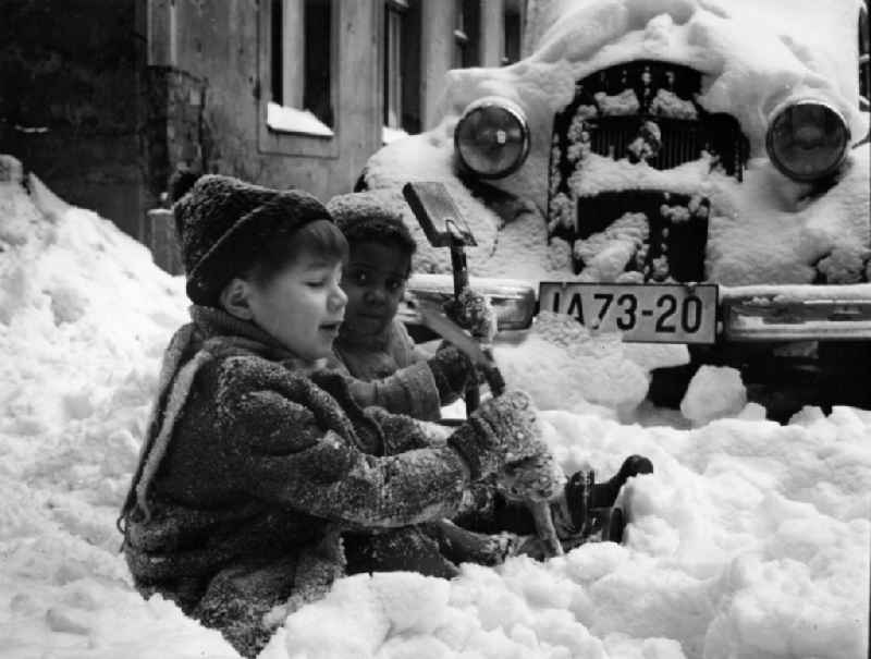 Two children sit in the street edge in the snow in Berlin, the former capital of the GDR, German democratic republic