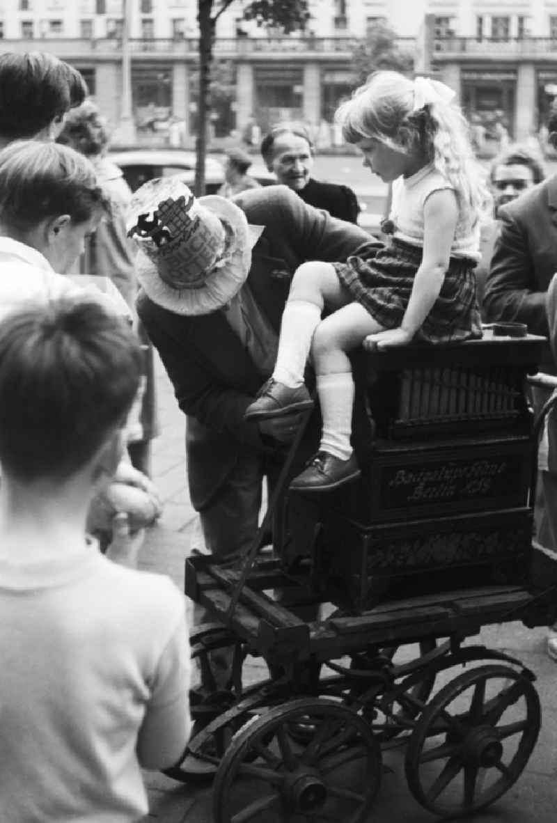 A small girl with plait sit on a barrel organ in Berlin, the former capital of the GDR, German democratic republic