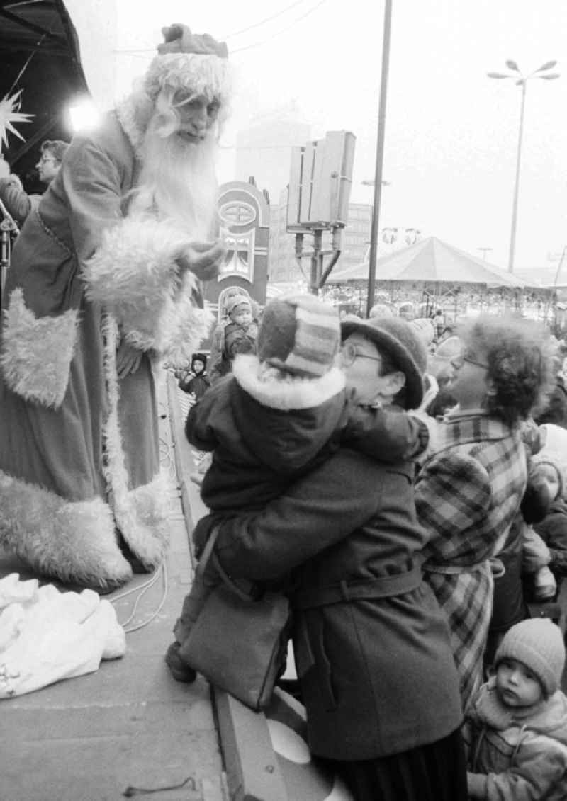 A mother lifts her child on the stage to the Santa Claus on the Berlin Christmas fair in Berlin, the former capital of the GDR, German democratic republic. Today there stands at this point the shopping centre 'Alexa'