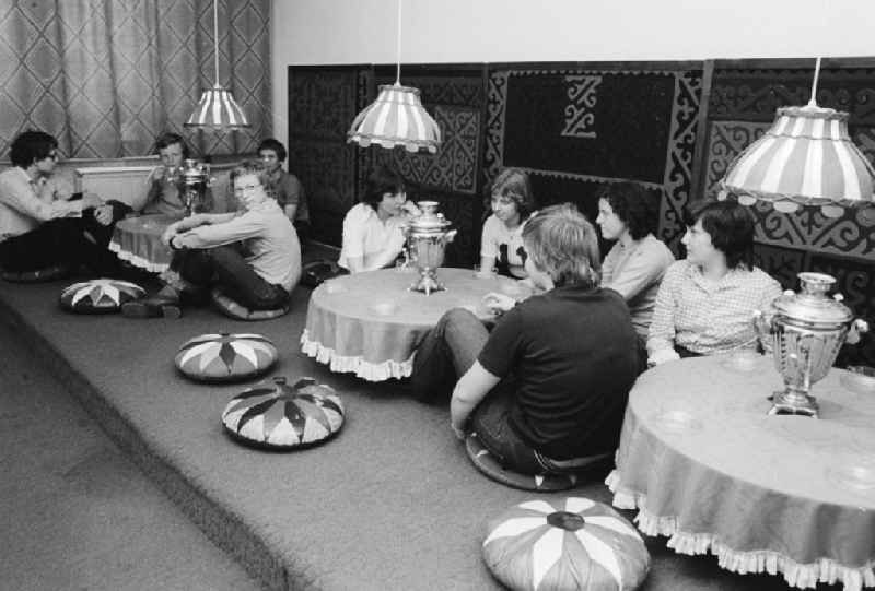 Youngsters sit on the ground in the 'tearoom' at the youth tourist's hotel 'Egon Schultz' in the animal park in Berlin, the former capital of the GDR, German democratic republic. Samovars with warm tea stand on the tables. Today one says animal park ABACUS hotel
