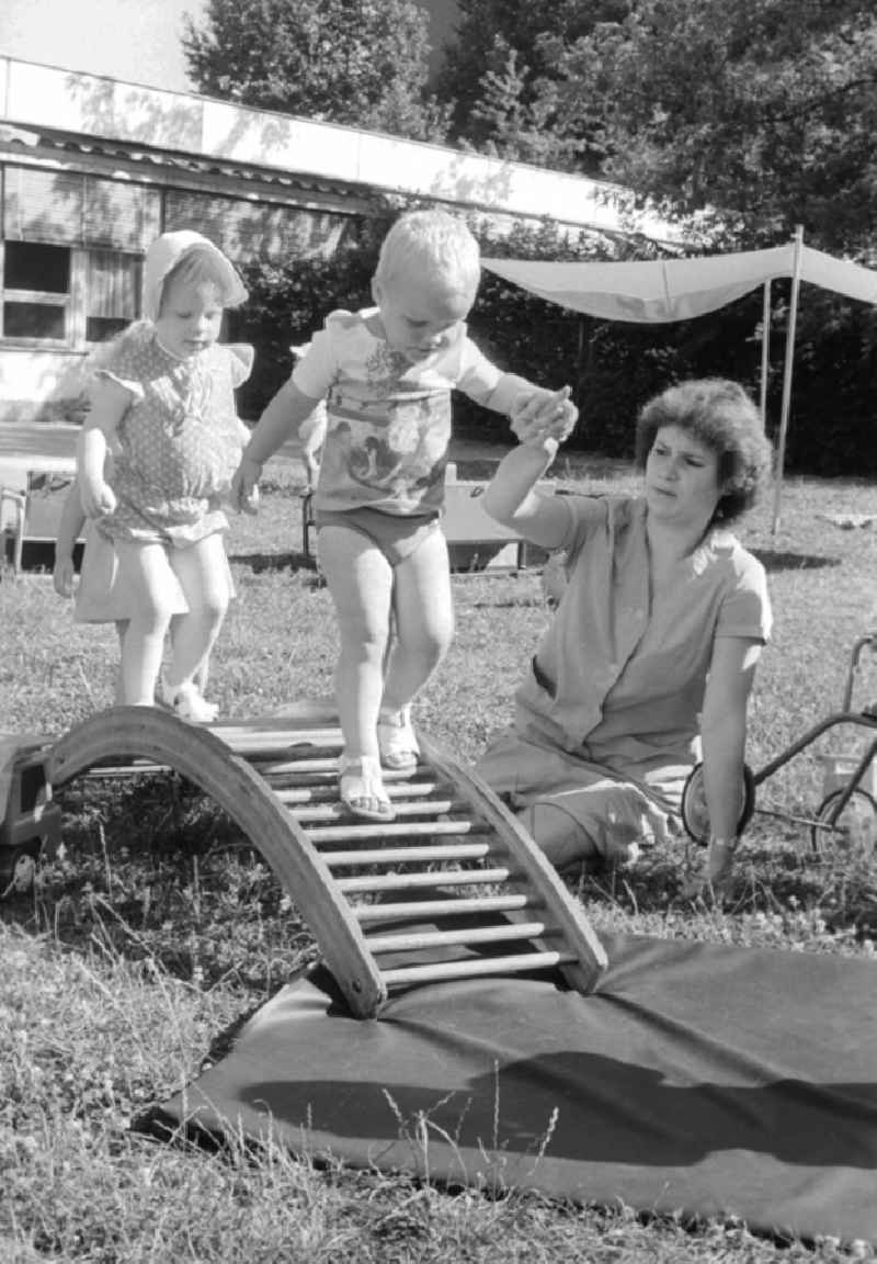 Children play together with her educator in the garden and do gymnastics about a wooden rung curve in Berlin, the former capital of the GDR, German democratic republic