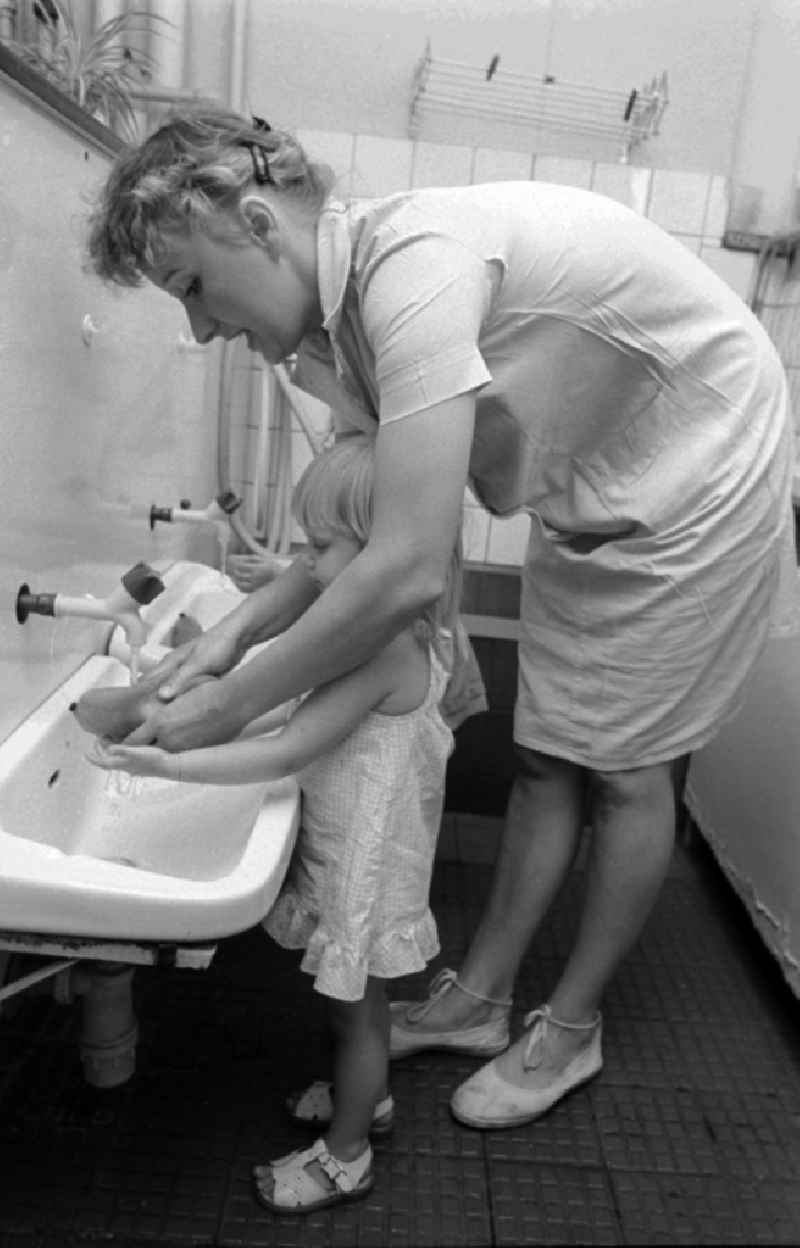 The educator helps children in the hand wash in the wash basin in a children cooked in Berlin, the former capital of the GDR, German democratic republic