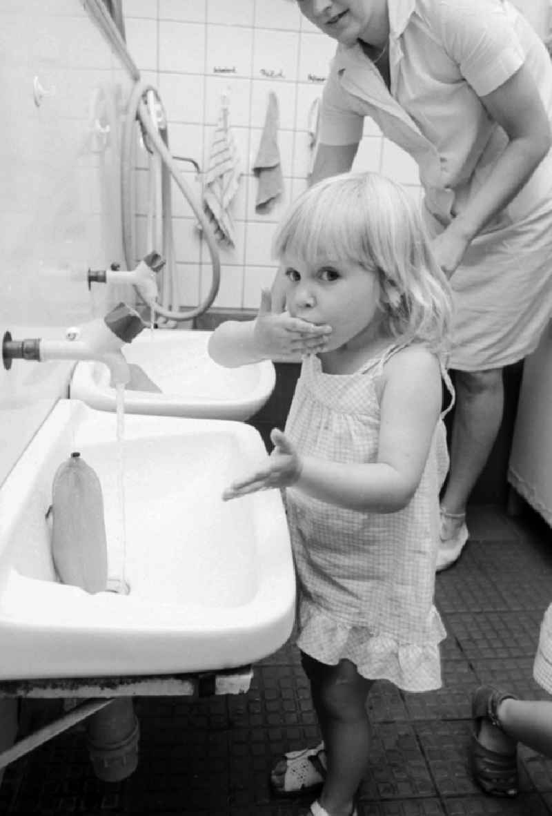 The educator helps children in the hand wash in the wash basin in a children cooked in Berlin, the former capital of the GDR, German democratic republic