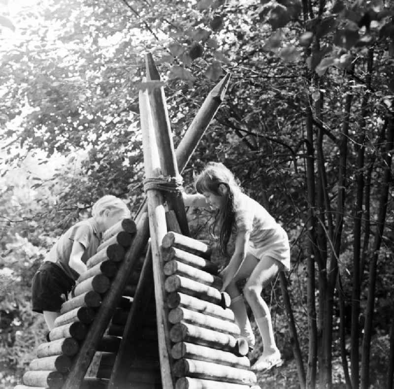 Children play playfully on a wooden tepee on a playground in Berlin, the former capital of the GDR, German democratic republic