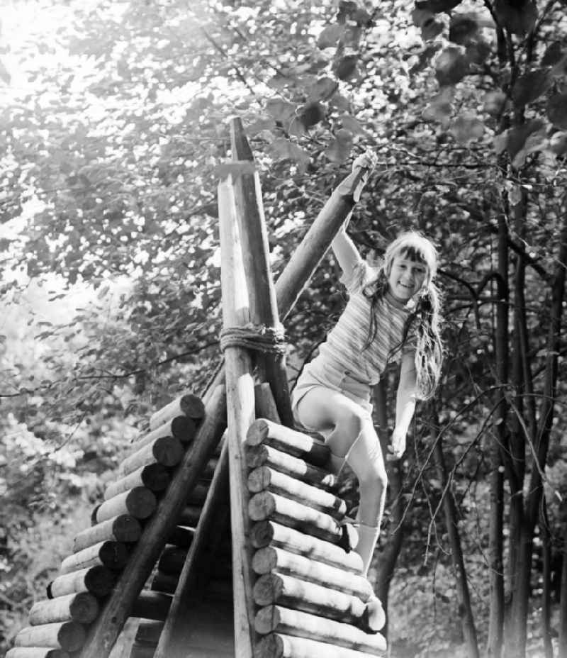 Laughing girl on a wooden tepee on a playground in Berlin, the former capital of the GDR, German democratic republic