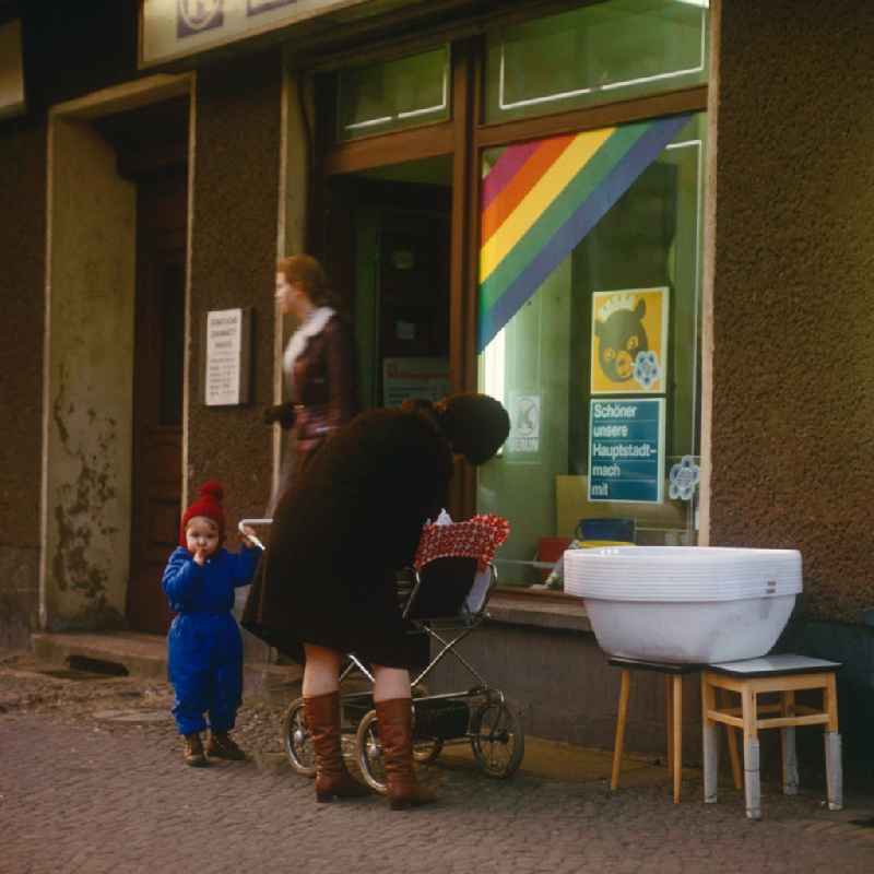 Mother by baby carriage and a toddler before a HO business for household articles in Berlin, the former capital of the GDR, German democratic republic