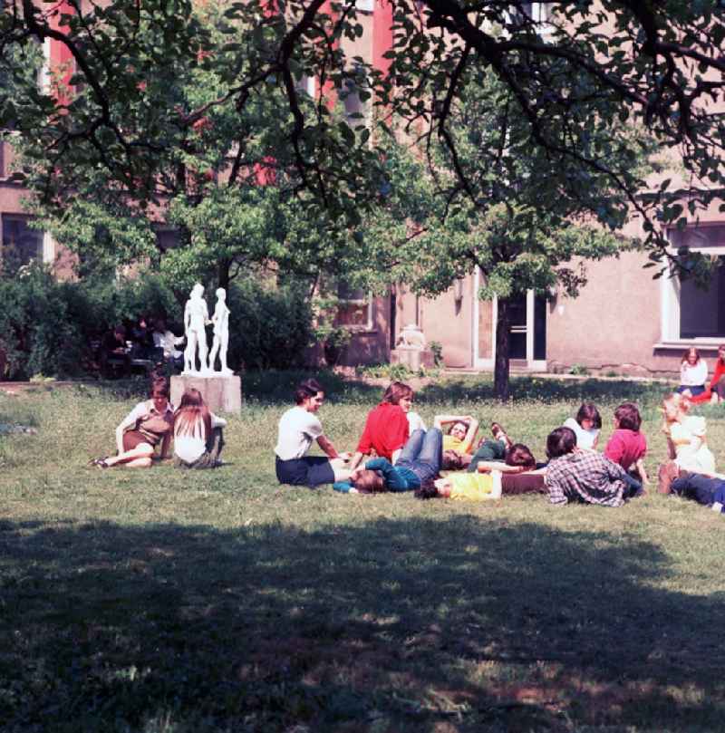 Students of the art college of Berlin white lake lie in the inner courtyard on the meadow and enjoy the sun in Berlin, the former capital of the GDR, German democratic republic