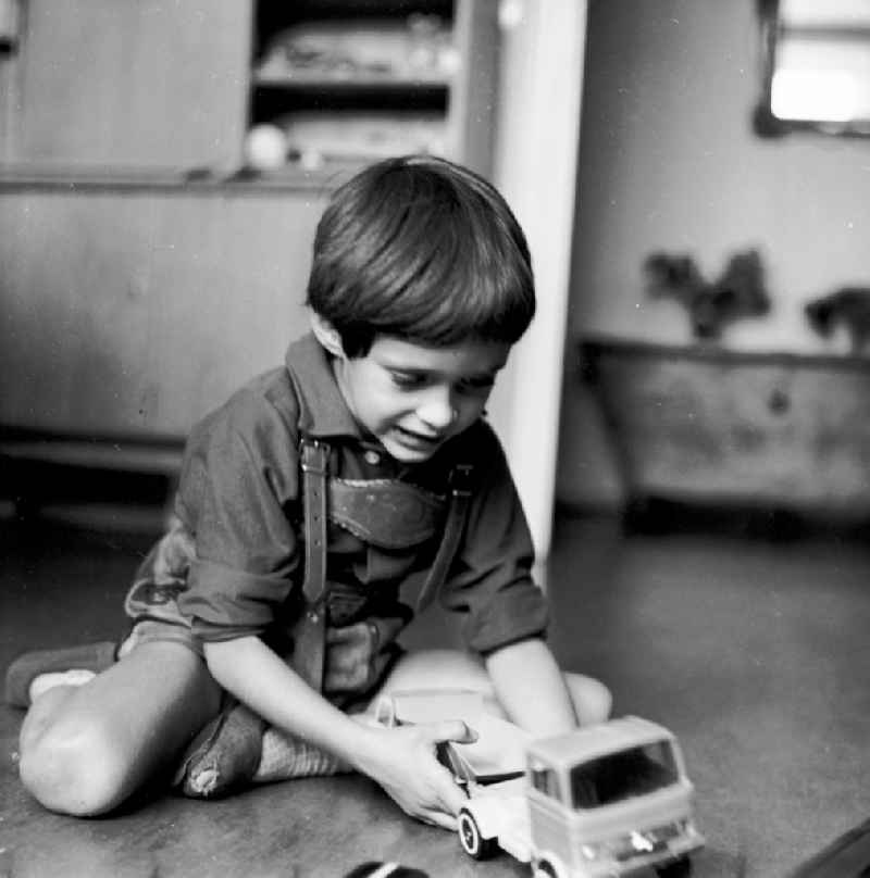 A small boy with leather trousers plays by his toys cars on the floor in Berlin, the former capital of the GDR, German democratic republic