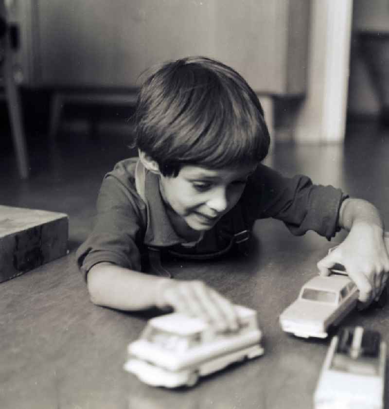 A small boy with leather trousers plays by his toys cars on the floor in Berlin, the former capital of the GDR, German democratic republic