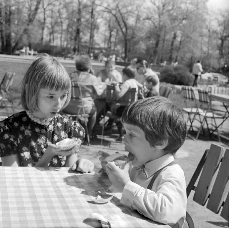 A brothers and sisters pair / children sit at a table in an open air restaurant and eat an ice in Berlin, the former capital of the GDR, German democratic republic