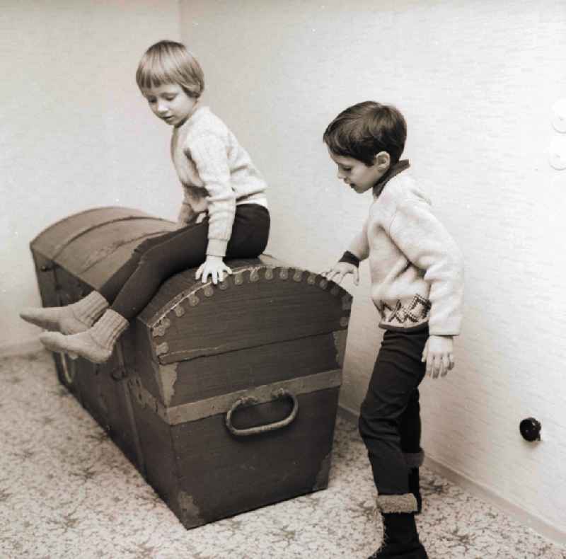 Two children sit on a big old wooden chest / wooden box in Berlin, the former capital of the GDR, German democratic republic