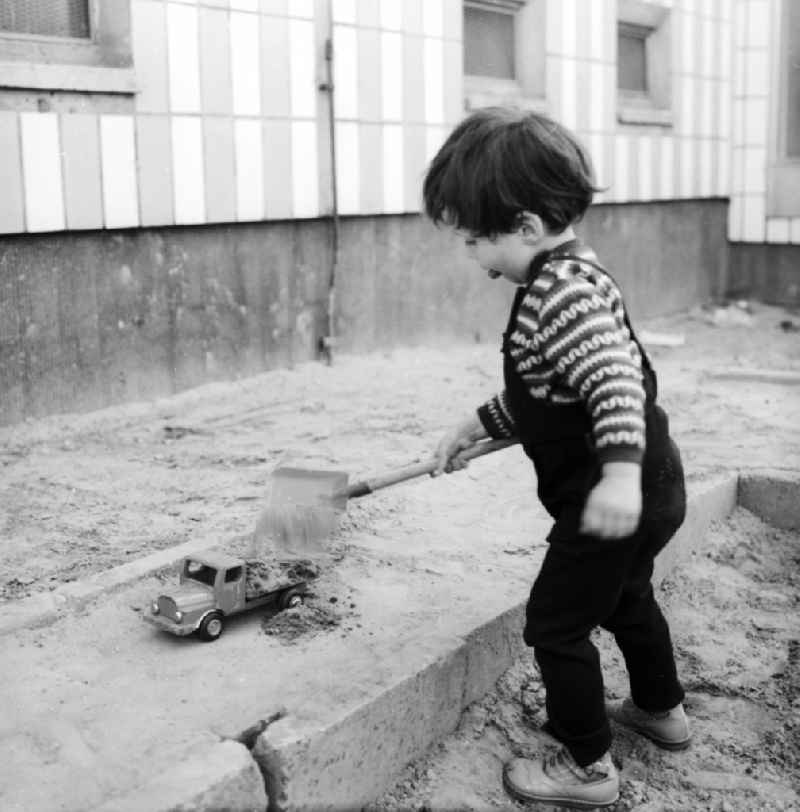 A small boy plays in the sandpit by a toys car in Berlin, the former capital of the GDR, German democratic republic