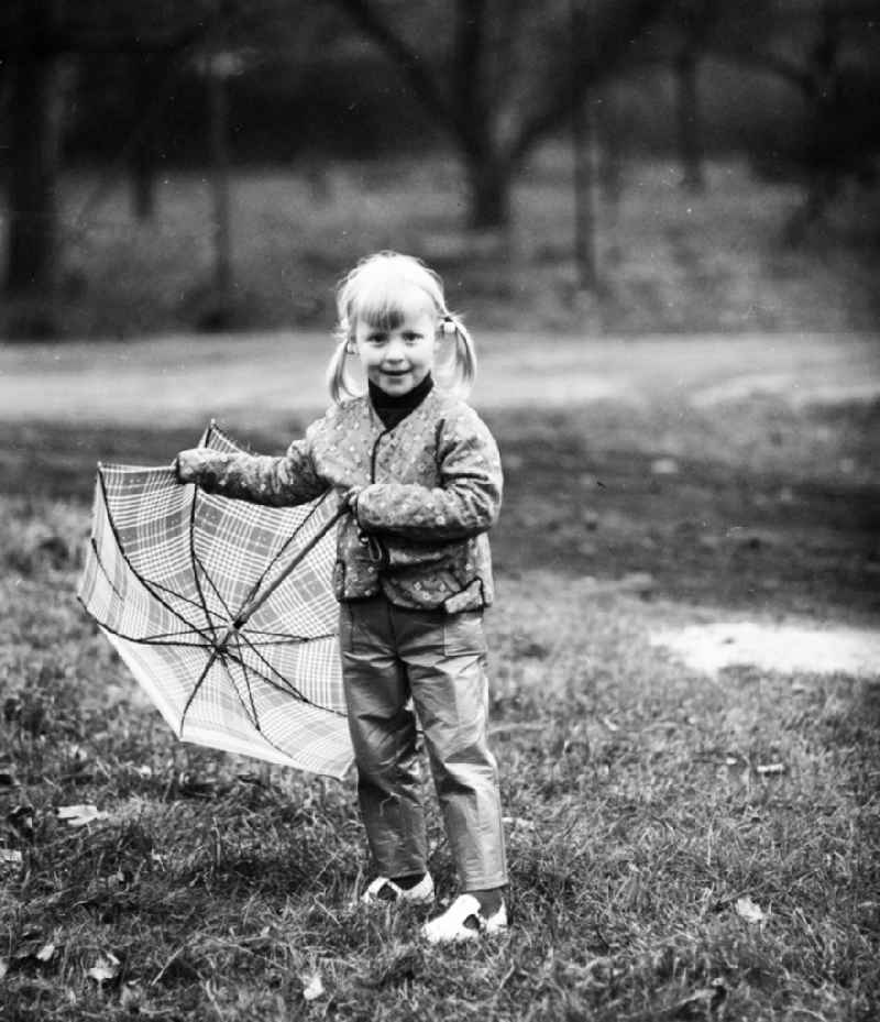A small girl with plaits stands with an umbrella on a meadow in Berlin, the former capital of the GDR, German democratic republic