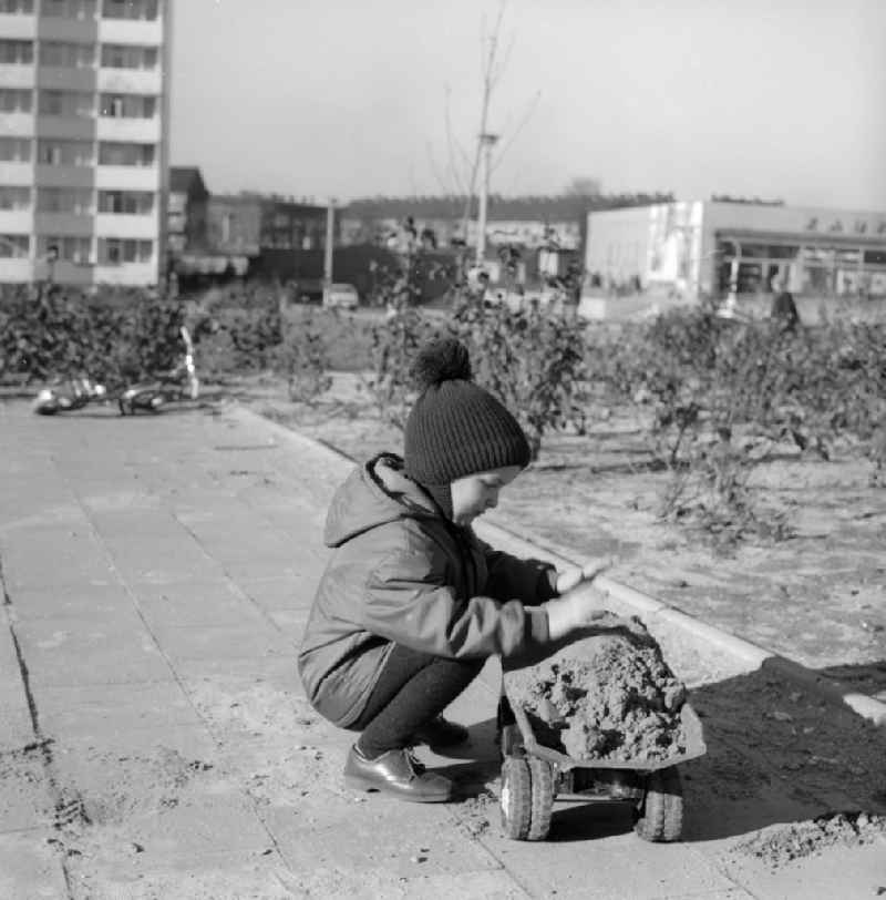 A little boy in a poodle cap plays with his plastic truck in the sandbox in a courtyard of a residential area in Berlin, the former capital of the GDR, German Democratic Republic