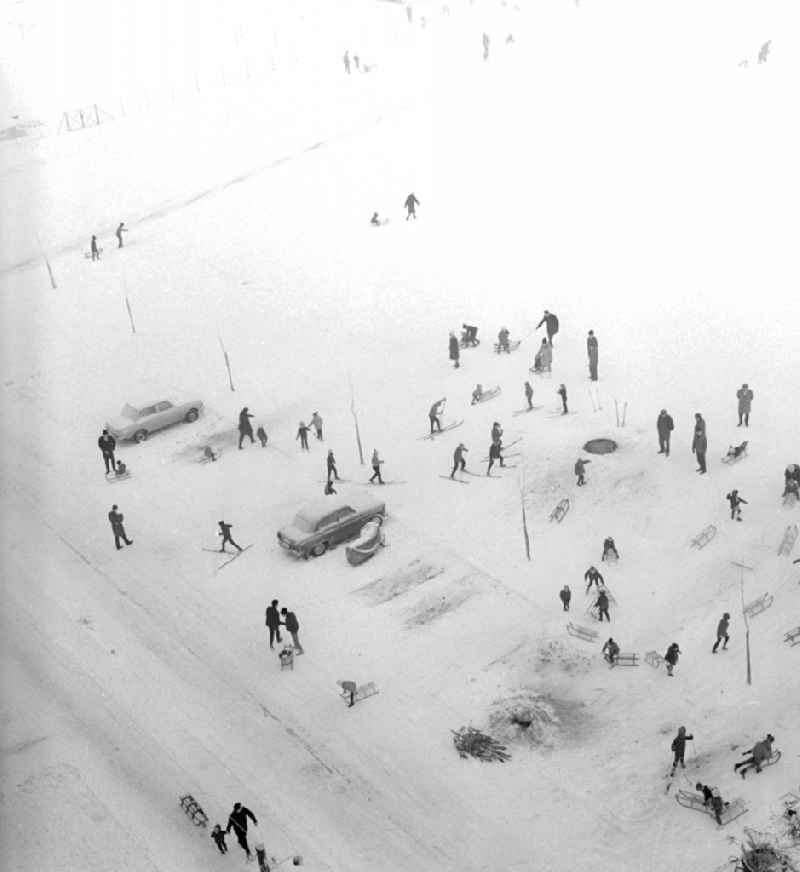 Children with sledges and skis on a snowy parking lot in a residential area in Berlin, the former capital of the GDR, German Democratic Republic