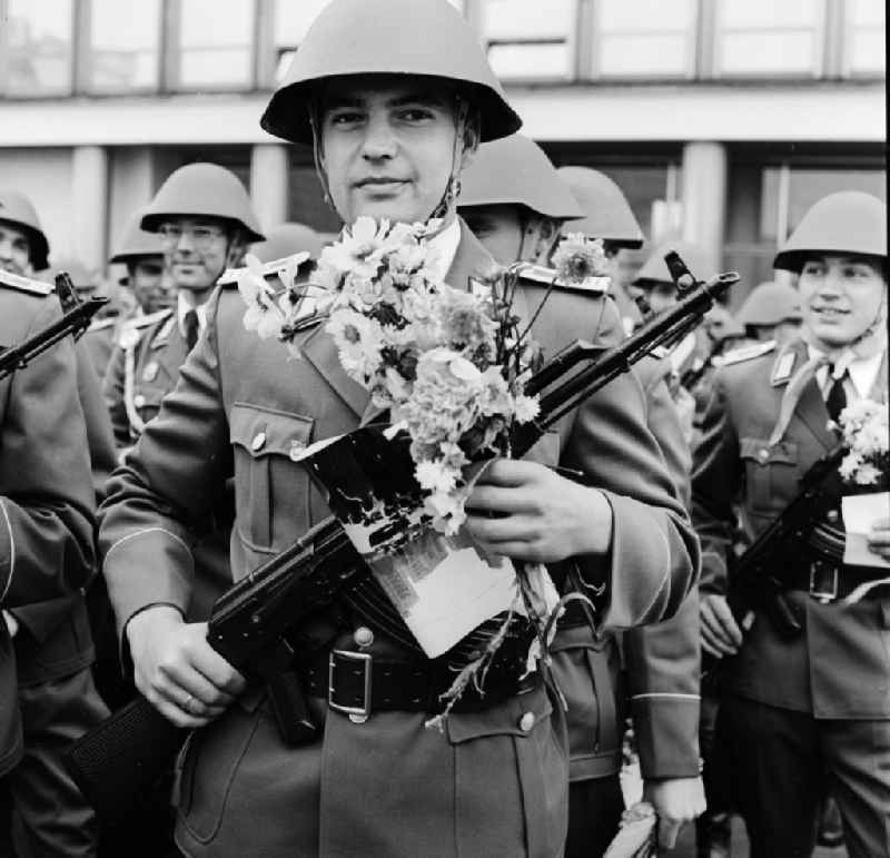 A soldier of the NVA with a steel helmet, an AK-47 assault rifle and flowers in his hand in Berlin, the former capital of the GDR, German Democratic Republic