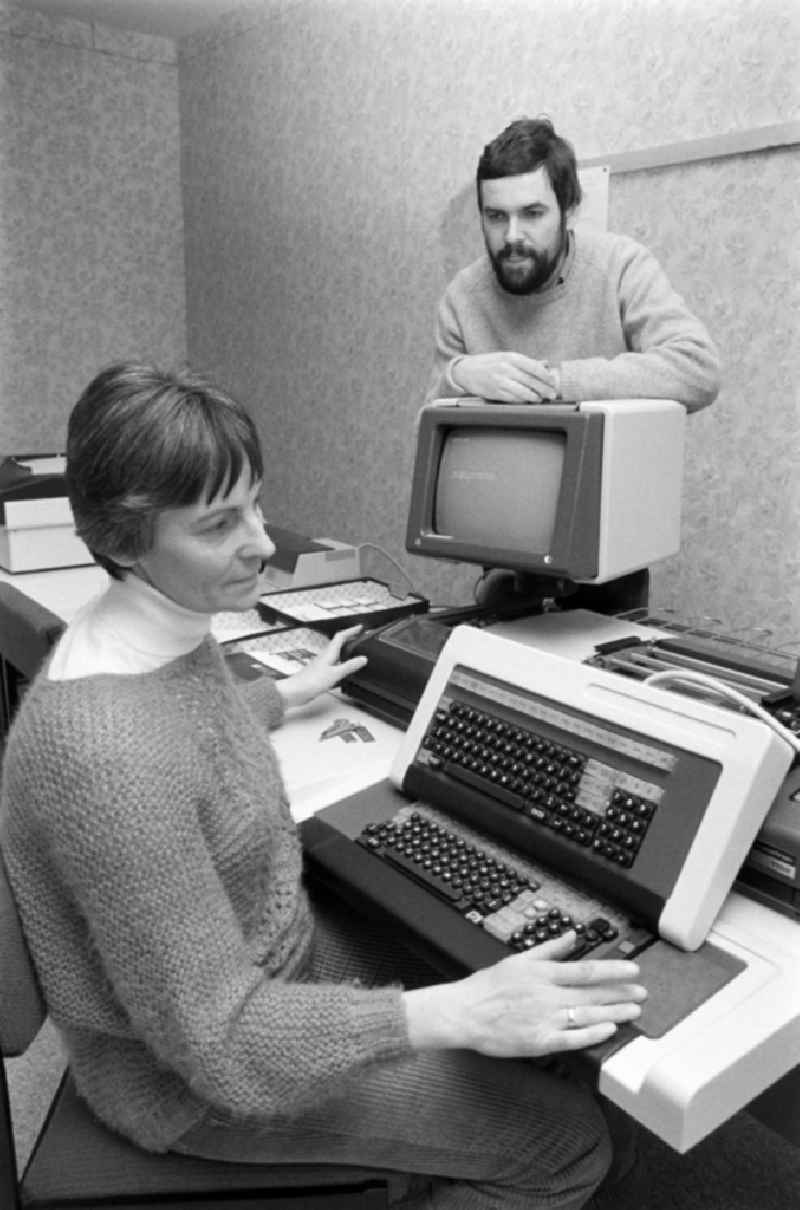 Employee at the project planning in the VEB Baukombinat Koepenick in the district Treptow-Koepenick in Berlin, the former capital of the GDR, German Democratic Republic. Woman sits in front of a Robotron computer and man stands behind a screen / monitor