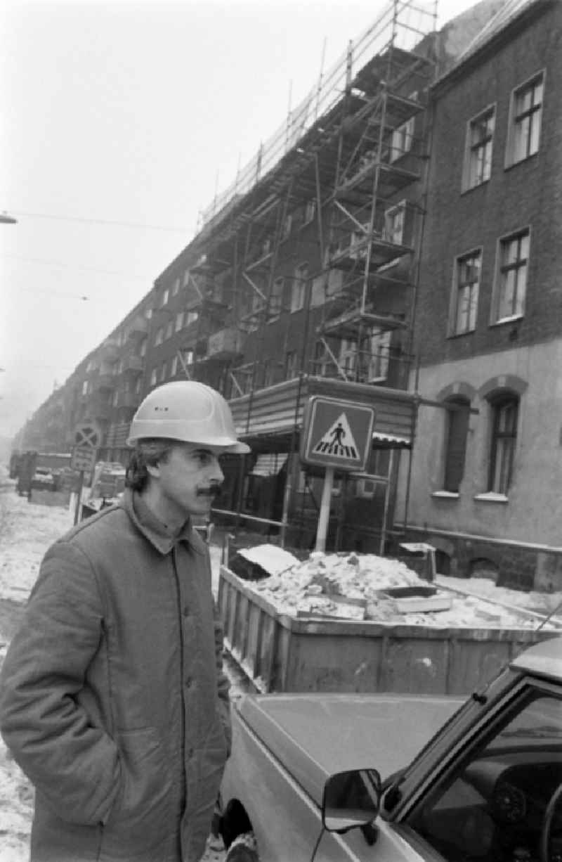 Construction worker with construction helmet stands on street Edisonstrasse in front of apartment building / residential building with scaffolding in the district of Treptow-Koepenick in Berlin, the former capital of the GDR, German Democratic Republic