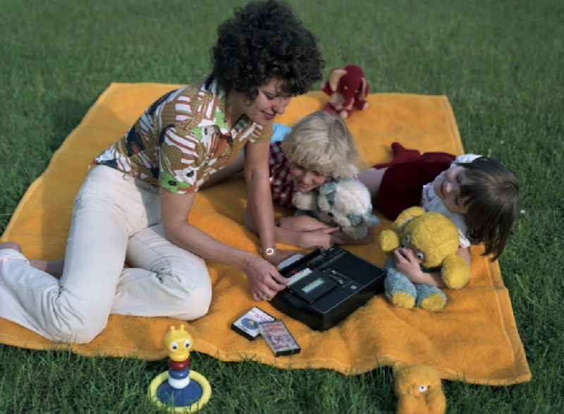 Young woman with child spends camping time in the park 'Monbijoupark' on a blanket with a radio recorder Anett IS of the VEB RFT Sternradio Berlin in the Mitte district of Berlin, the former capital of the GDR, German Democratic Republic