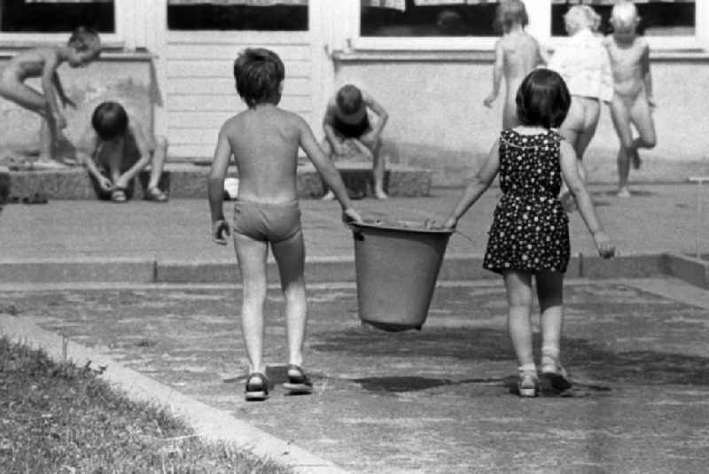 Boy and girl together carry a bucket in kindergarten in Berlin Eastberlin on the territory of the former GDR, German Democratic Republic