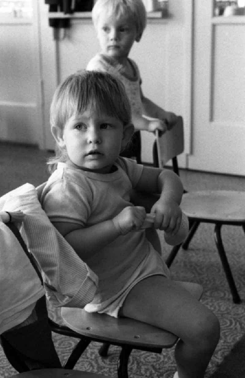 Preparing for a nap in the kindergarten in Berlin Eastberlin on the territory of the former GDR, German Democratic Republic. Toddler tries to undress on his own and pulls on his sock or stocking