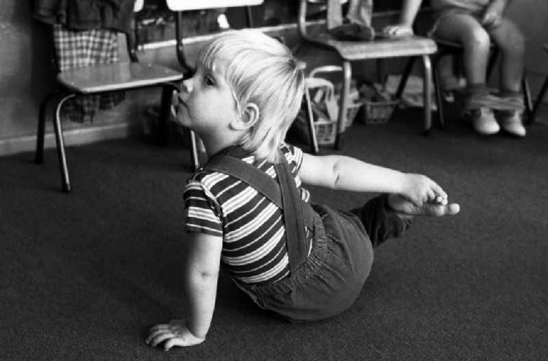 Preparing for a nap in the kindergarten in Berlin Eastberlin on the territory of the former GDR, German Democratic Republic. Toddler sitting on the floor