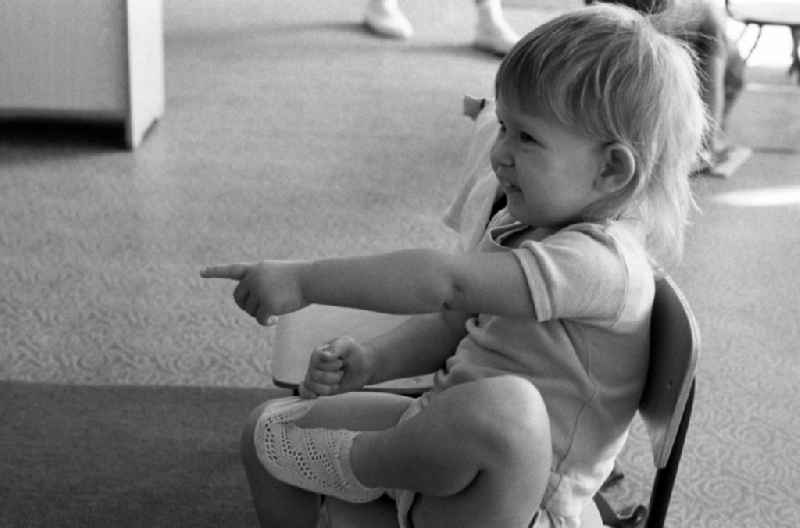 Preparing for a nap in the kindergarten in Berlin Eastberlin on the territory of the former GDR, German Democratic Republic. Toddler tries to undress on his own and takes off a sock or stocking in the process