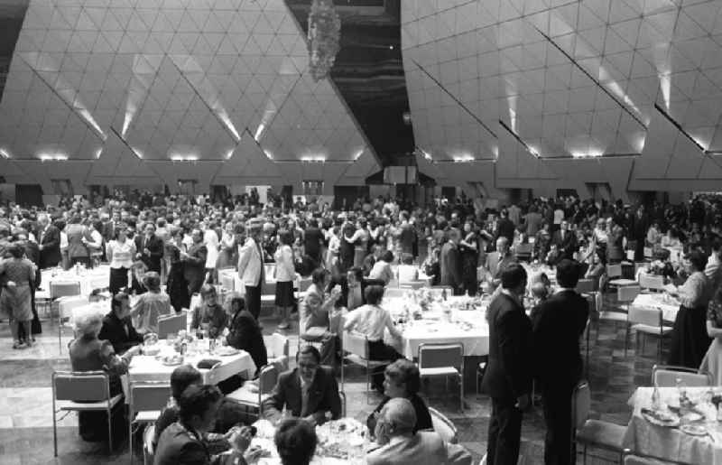 Guests at tables and dancing in the Great Hall at the Palace of the Republic in the district Mitte in Berlin Eastberlin on the territory of the former GDR, German Democratic Republic. The Palace of the Republic in the GDR was one of the largest and most modern multi-purpose cultural buildings of its kind in Europe. In addition to catering facilities, the building housed a large multi-purpose hall and the parliament building of the People's Chamber of the GDR. The Great Hall could be converted into a banquet hall, concert hall or event hall with a maximum of 5,00