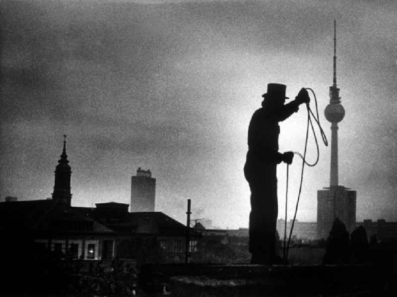 Chimney sweep in typical working clothes with equipment of his craft in Berlin Eastberlin on the territory of the former GDR, German Democratic Republic. In the background, the Berlin television tower