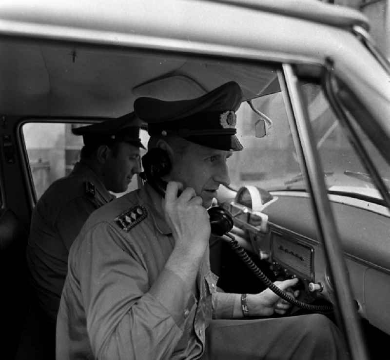 Policeman in uniform of the VP People's Police - Master Reinhold Guenther with a telephone receiver in a radio conversation in a radio patrol car GAZ M21 Volga in the district of Pankow in Berlin East Berlin on the territory of the former GDR, German Democratic Republic
