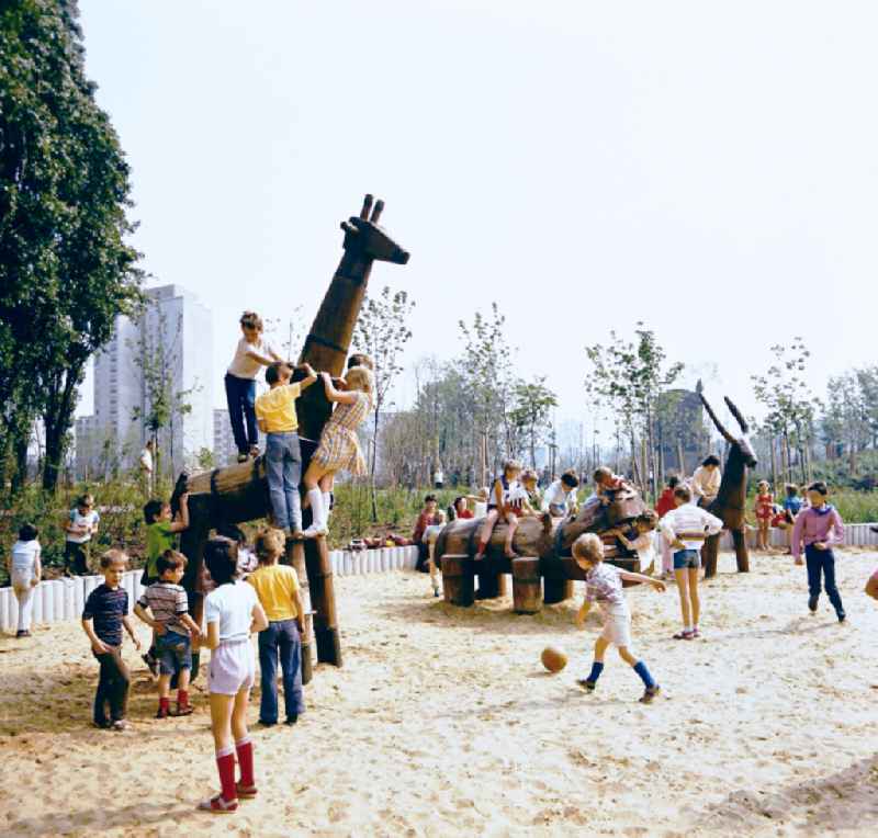 Children play on playground equipment such as giraffe, hippo and ibex at the playground in the residential area and park area Ernst-Thaelmann-Park Prenzlauer Berg in Berlin Eastberlin on the territory of the former GDR, German Democratic Republic