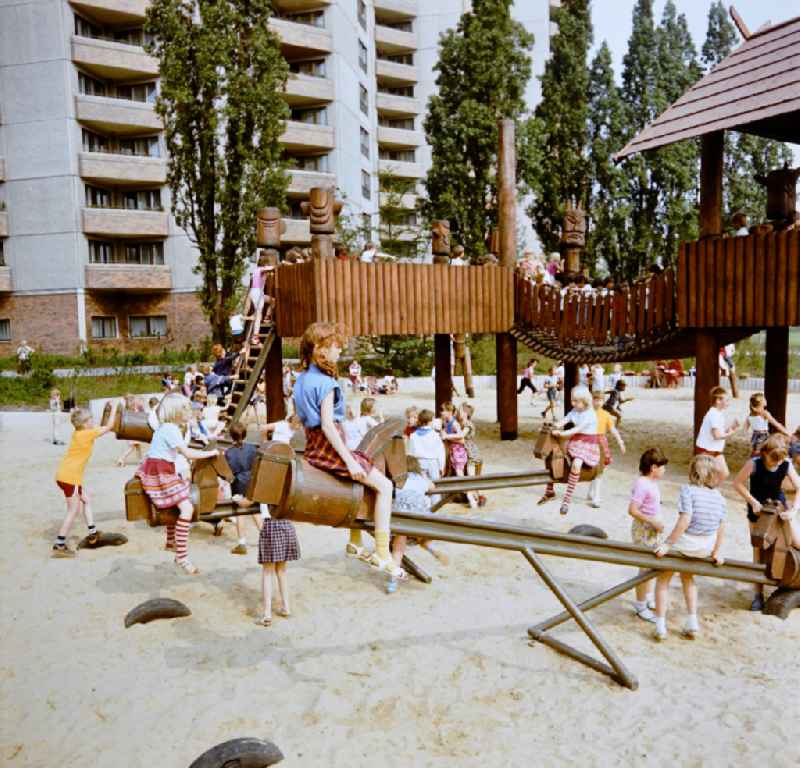Children play on playground equipment equipment like seesaws at the playground in the residential area and park area Ernst-Thaelmann-Park Prenzlauer Berg in Berlin Eastberlin on the territory of the former GDR, German Democratic Republic