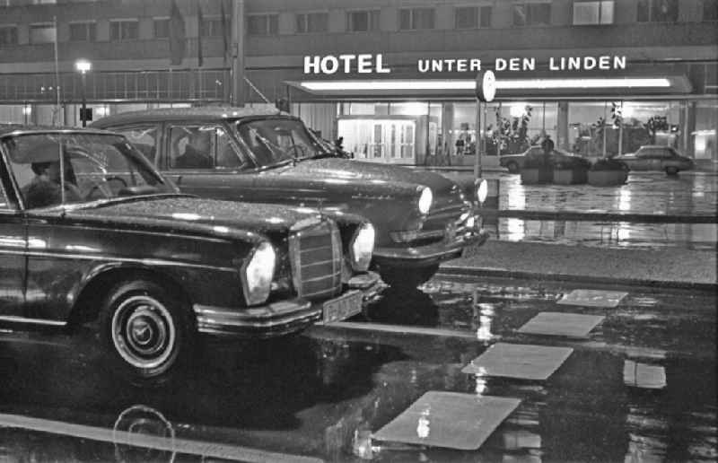 Car - motor vehicle in night traffic of the Mercedes type next to a GAZ M-21 Volga in front of the Hotel Unter den Linden on Friedrichstrasse in the district Mitte in Berlin East Berlin on the territory of the former GDR, German Democratic Republic