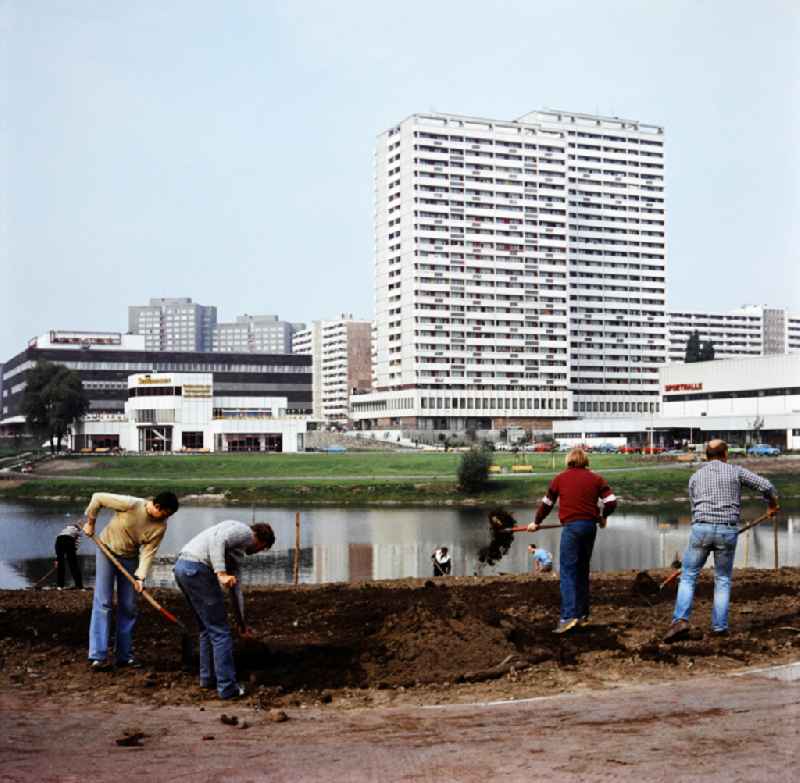 Fennpful park in the Lichtenberg district of Eastberlin in the territory of the former GDR, German Democratic Republic. Workers create a new flower bed at the lake. In the background are the lakeside terraces, the consumer department store, apartment buildings and a sports hall