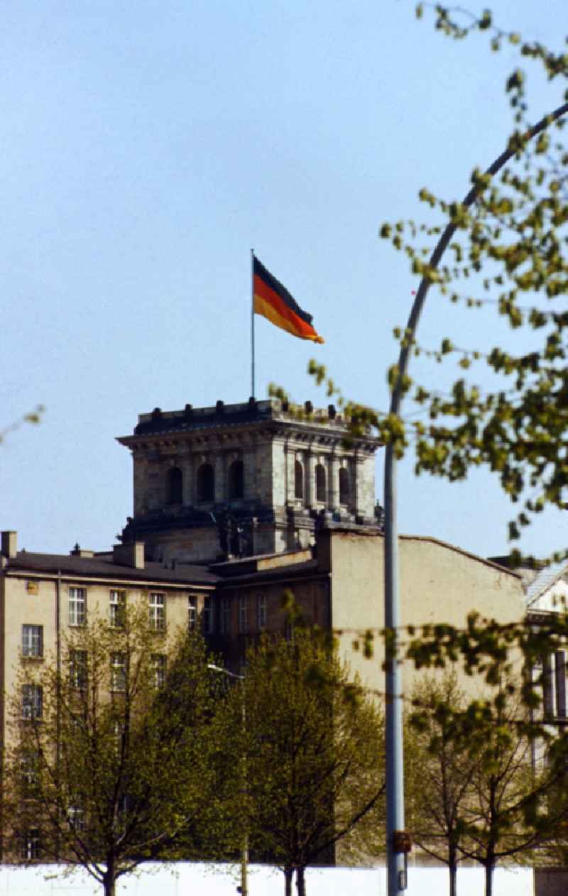 View over the wall towards the Reichstag with tower and Germany flag in Berlin-Mitte on the territory of the former GDR, German Democratic Republic