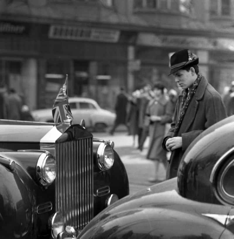 Young man in a hat stands in front of a car with the national flag of Great Britain on the car radiator in Berlin in the territory of the former GDR, German Democratic Republic