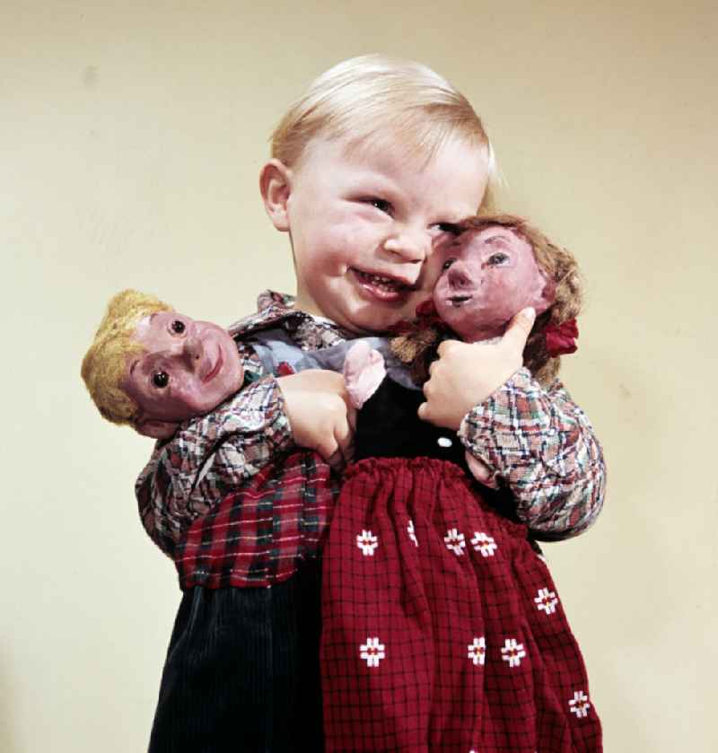 A boy with blond hair holds the hand puppets Kruemel (girl) and Flax (boy) in East Berlin on the territory of the former GDR, German Democratic Republic