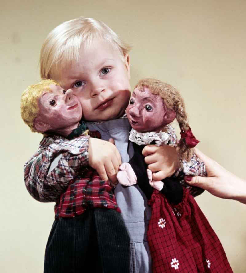 A boy with blond hair holds the hand puppets Kruemel (girl) and Flax (boy) in East Berlin on the territory of the former GDR, German Democratic Republic
