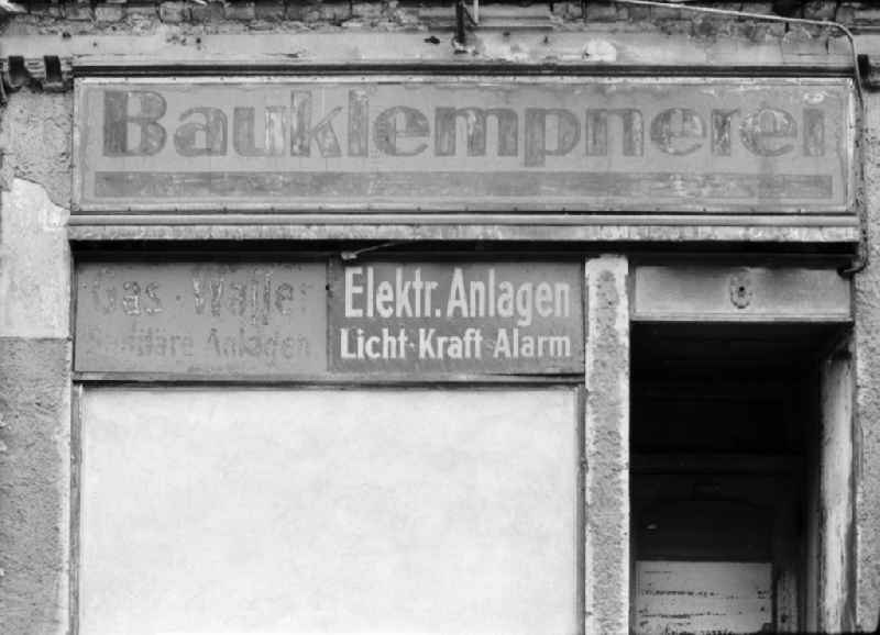 Fading lettering in the entrance area and shop window of a retail store 'Bauklempnerei - Gas - Wasser - Elektrische Anlagen' in the street area of an old residential building facade on Schwedter Strasse in the district of Prenzlauer Berg in Berlin East Berlin in the area of the former GDR, German Democratic Republic
