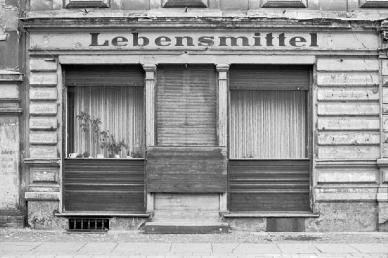 Fading lettering in the entrance area and shop window of a retail store ' Lebensmittel ' in the street area of an old residential building facade on street Jessnerstrasse in the district Friedrichshain in Berlin Eastberlin on the territory of the former GDR, German Democratic Republic