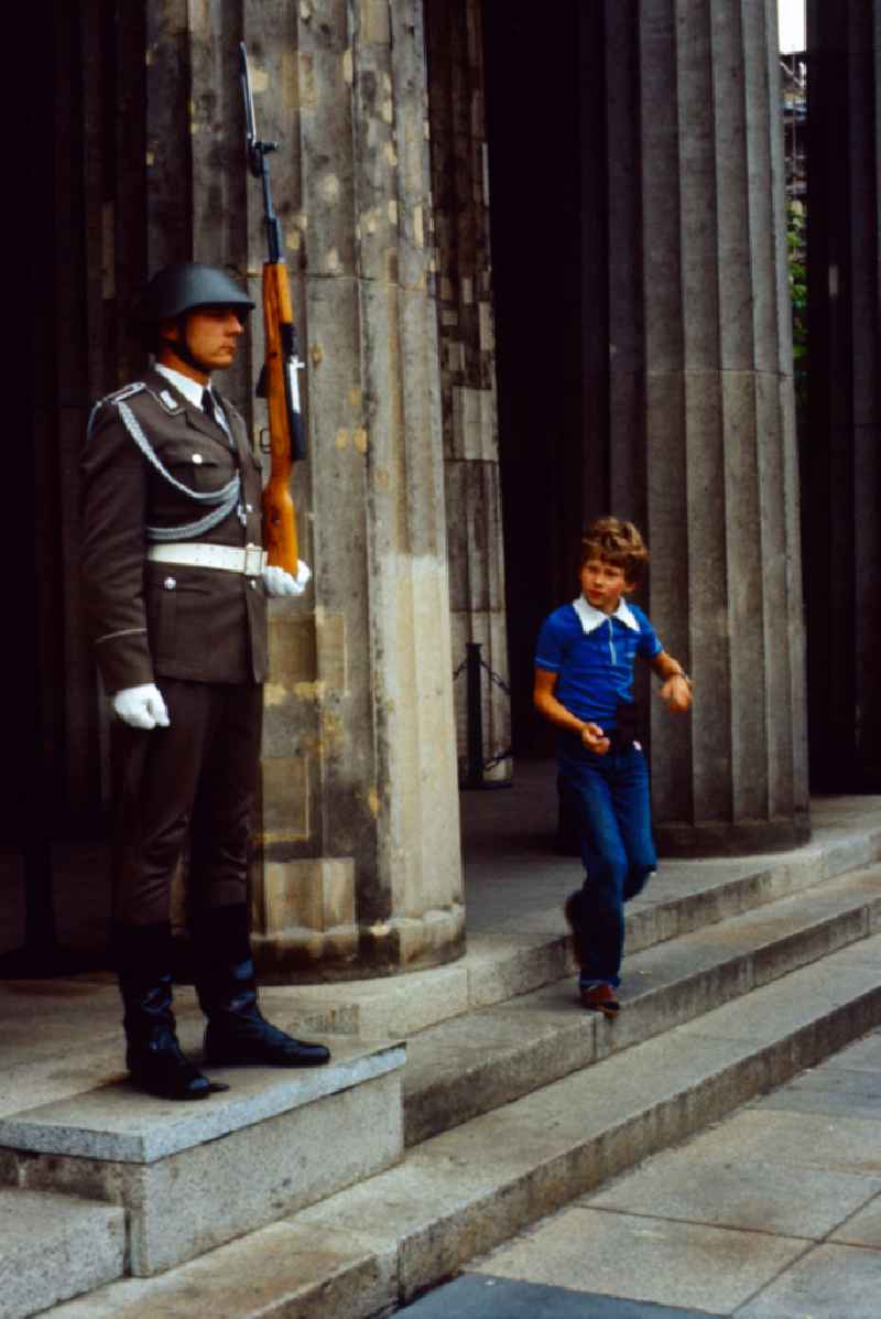 New Guard on the boulevard Unter den Linden by Karl Friedrich Schinkel in Berlin in the GDR. Boy runs past a soldier of the NVA guard of honour