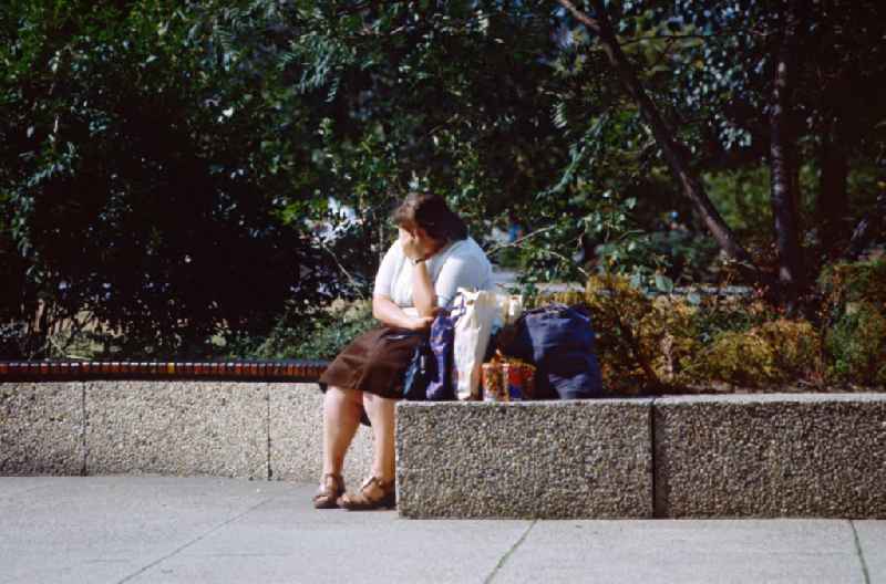 Woman taking a break with full shopping bags on a park bench in East Berlin on the territory of the former GDR, German Democratic Republic