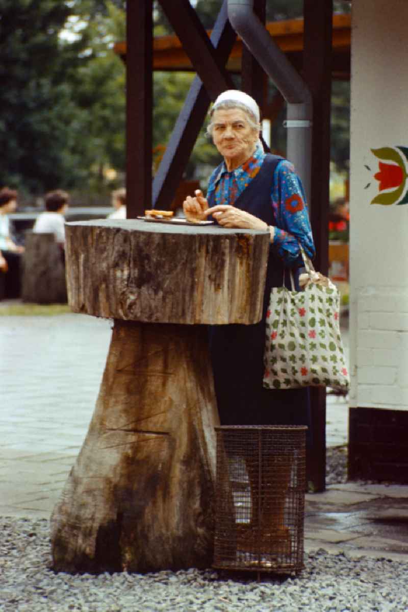 Old woman eating a currywurst in East Berlin on the territory of the former GDR, German Democratic Republic
