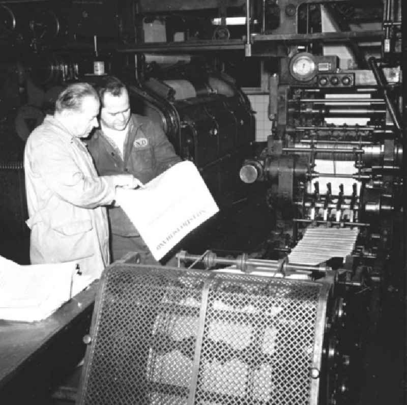 Arbeiter stehen an Rotationsdruckmaschine / Druckmaschine und begutachten die aktuelle Ausgabe der Zeitung ND 'Neues Deutschland'.