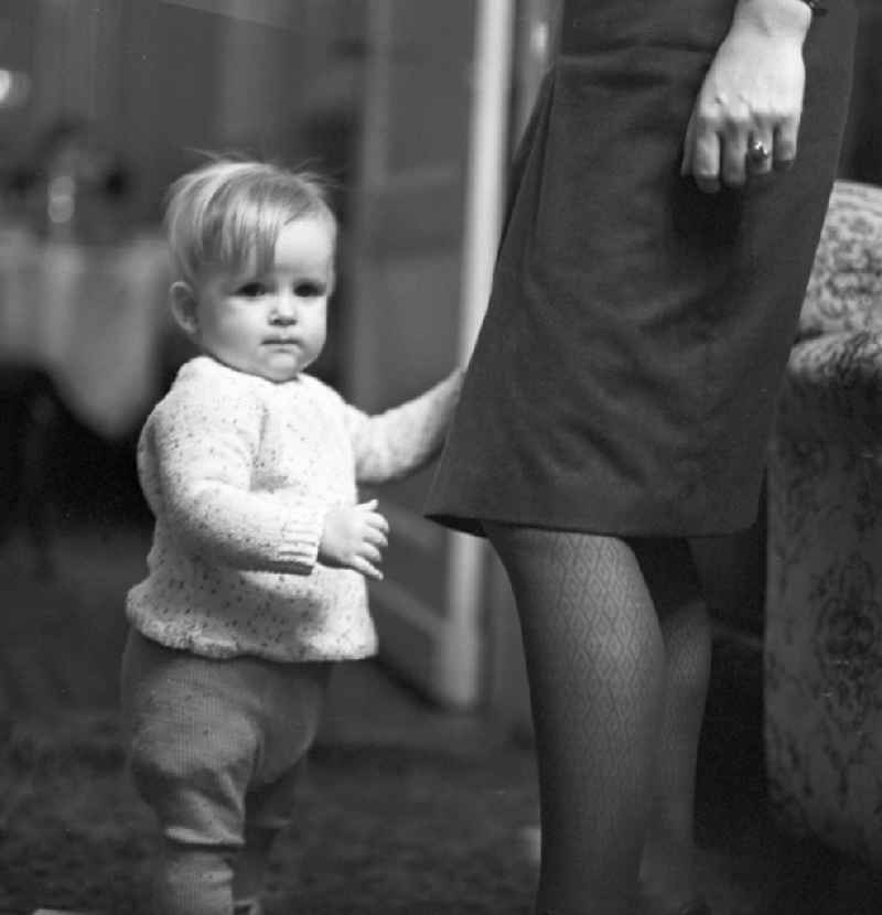 A young boy clings to the skirt of his mother