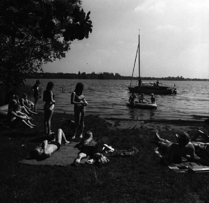 Campingurlaub am Krossinsee. Im Bild: Urlauber beim Baden und Sonnen. Im Hintergrund ein Schlauchboot und ein auslaufendes Segelschiff.