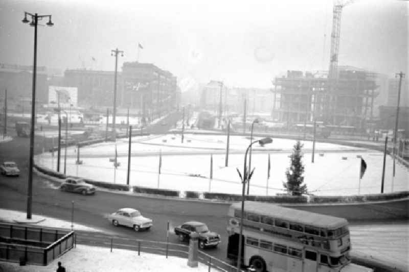 Verschneiter Kreisverkehr auf dem Alexanderplatz. Bus biegt ab, Autos fahren auf Straße. Baustelle Haus des Lehrers mit Kran im Hintergrund.
