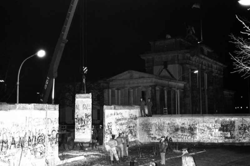 Nachtaufnahme: Maueröffnung / Mauerabbau am Brandenburger Tor. Kran hebt Mauerstück / Mauersegment.