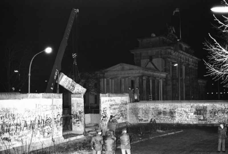 Nachtaufnahme: Maueröffnung / Mauerabbau am Brandenburger Tor. Kran hebt Mauerstück / Mauersegment.
